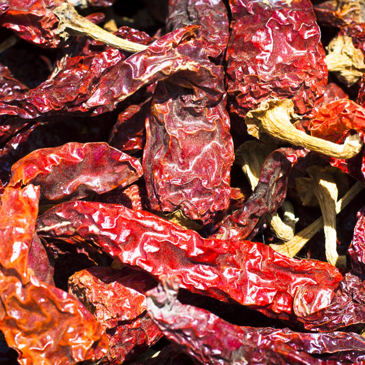 A close-up of whole dried Kashmiri chilli pods showing their wrinkled skin, elongated shape and rich deep red colouring.