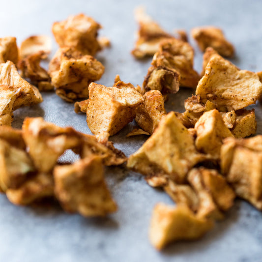 A close-up of Organic Apple Pieces Dried scattered on a surface, showing their chopped shape, golden-brown colouring and naturally dried texture.