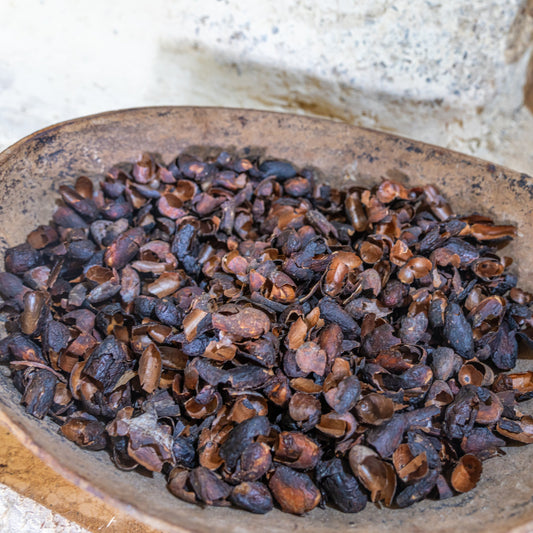 A close-up of Organic Cacao Husks in a rustic bowl, showing the curled dried pieces and their natural deep brown colouring and texture.