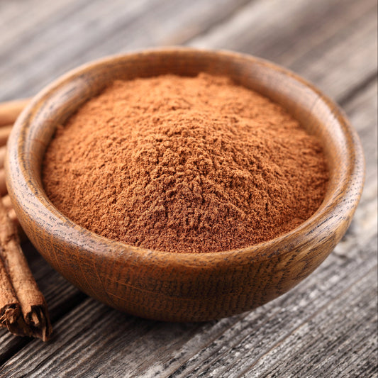 Organic Ceylon Cinnamon Powder fills a wooden bowl on a rustic surface, showing its finely ground texture and natural warm brown colouring.