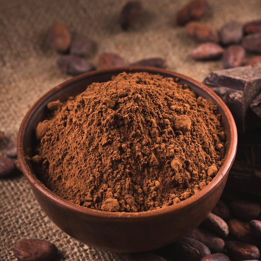Organic cocoa powder fills a small brown bowl surrounded by cocoa beans, showing the fine texture and rich dark brown colour of the powder.