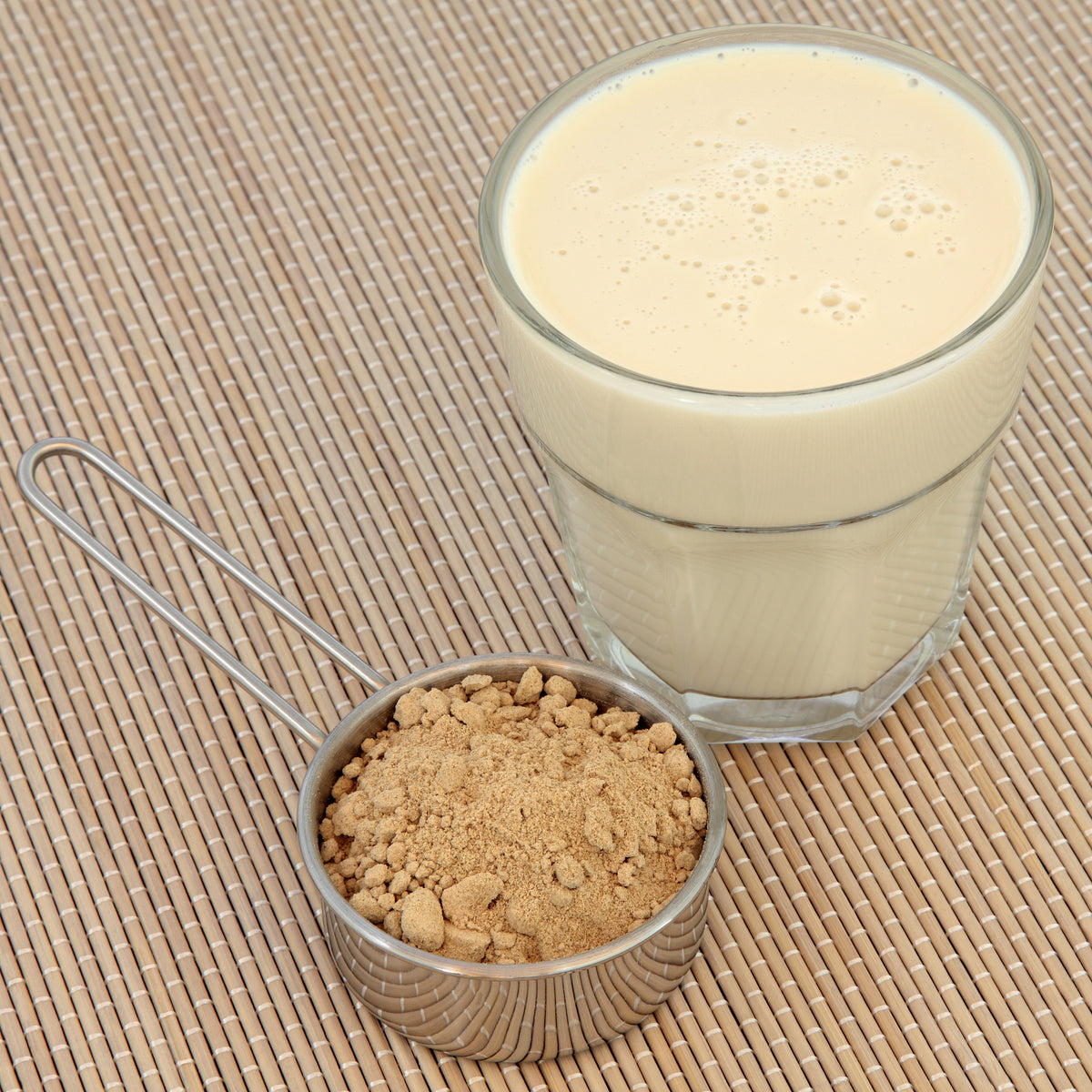 A creamy maca drink is served in a clear glass beside a small bowl of maca powder, showing a simple drink preparation using Organic Maca Powder.