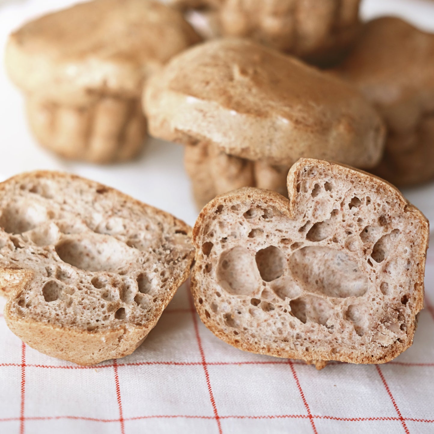 Sliced rustic bread with a porous crumb sits beside whole bread rolls, showing a baking use for The Herb Shed Organic Psyllium Husk.