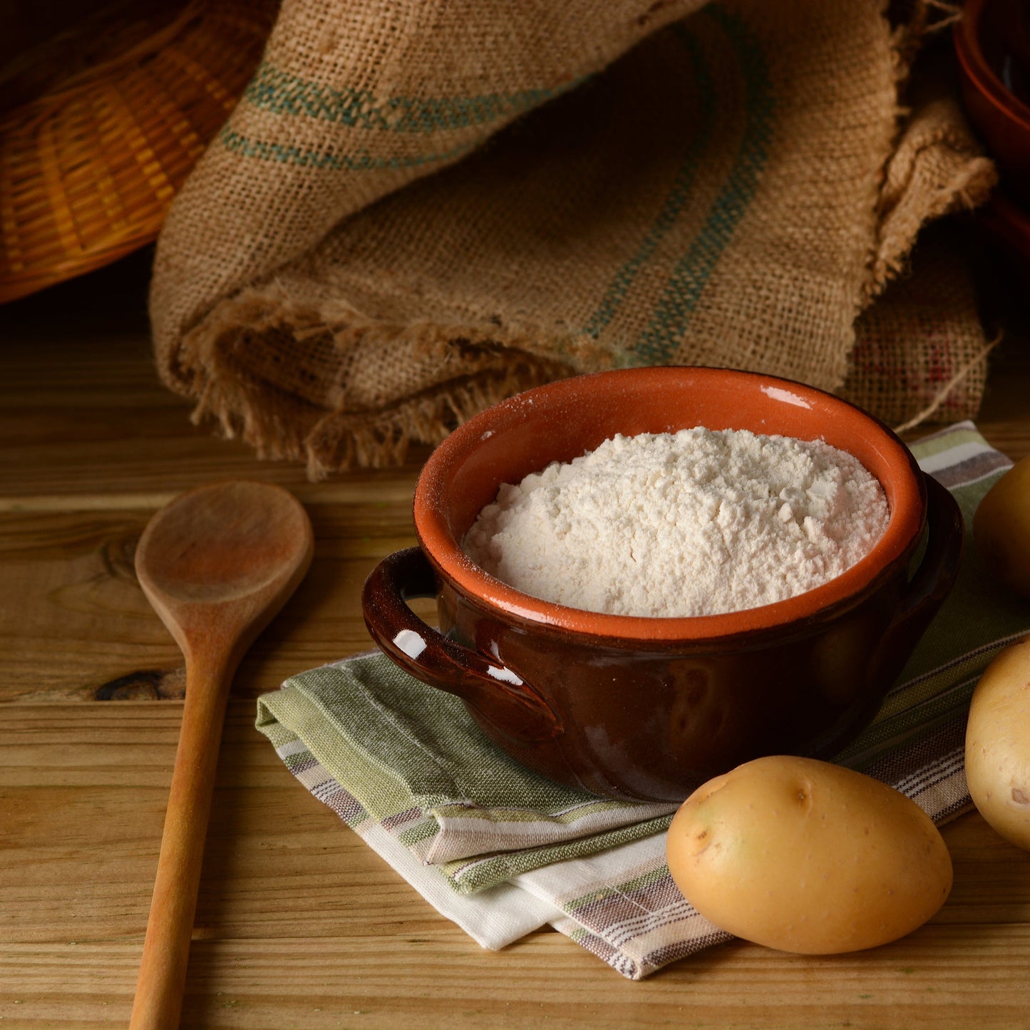 Potato starch flour sits in a small bowl on a rustic wooden surface with eggs, a scoop and baking ingredients arranged nearby.