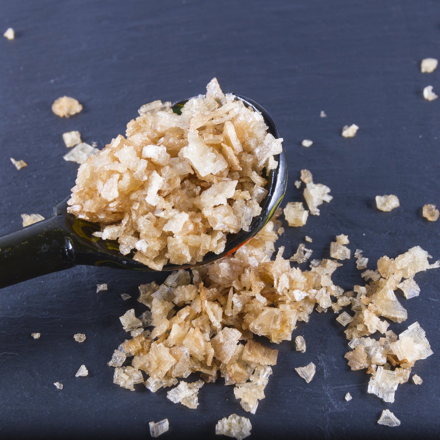 Cold-smoked sea salt flakes on a spoon, scattered across a dark slate surface – The Herb Shed Wollongong