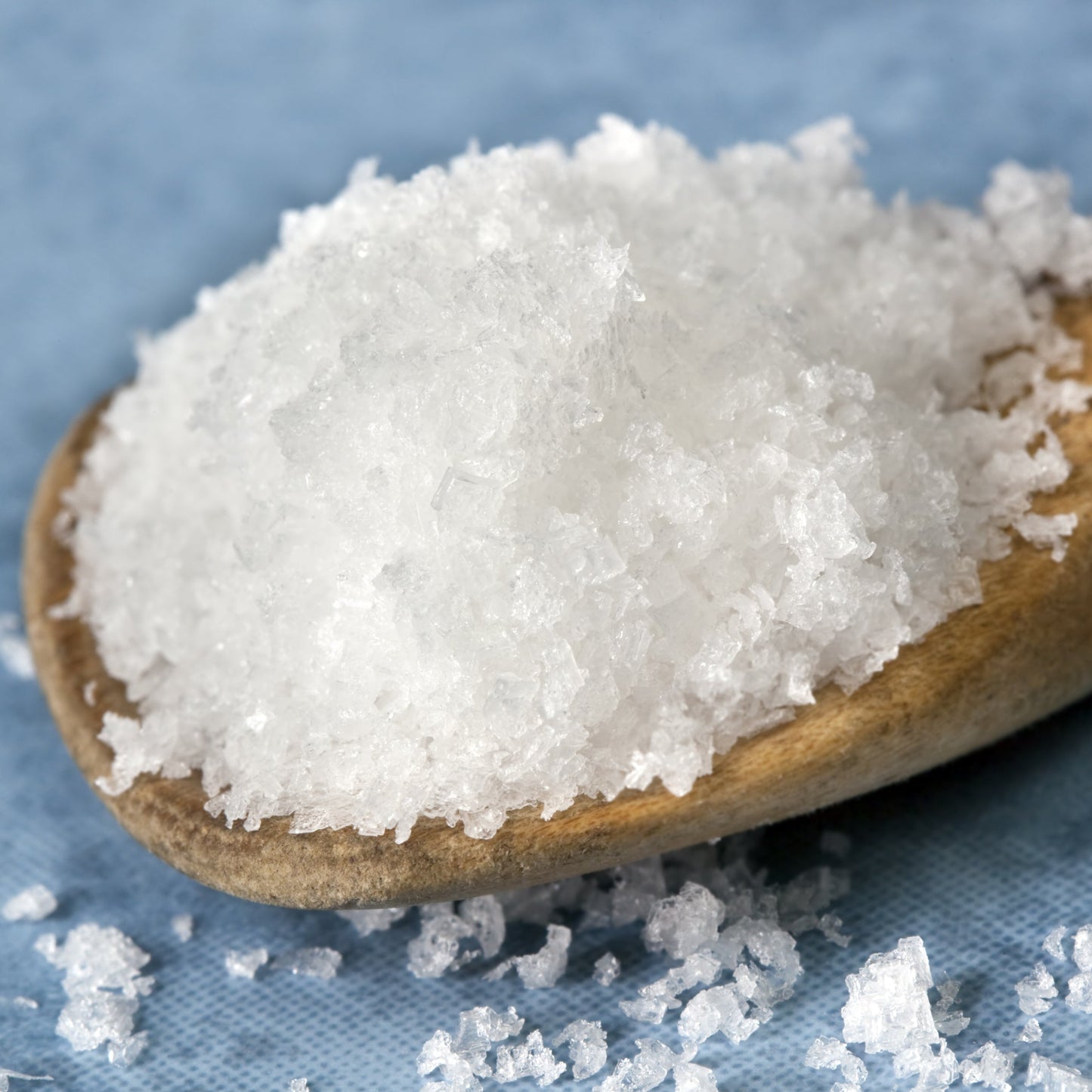 Close-up of sea salt flakes on a wooden spoon with a blue background – crisp mineral salt from The Herb Shed Wollongong