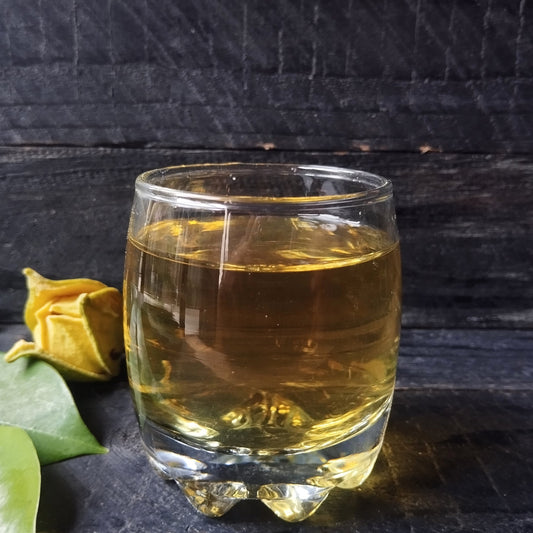 Glass of freshly brewed soursop leaf tea with a warm amber hue, with loose dried leaves beside the cup on a white background – The Herb Shed Wollongong