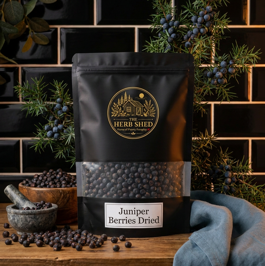 A black stand-up pouch of Herb Shed Juniper Berries Dried, displayed on a rustic wooden table with loose berries, a stone mortar, and blueberries in a dark tiled kitchen setting.