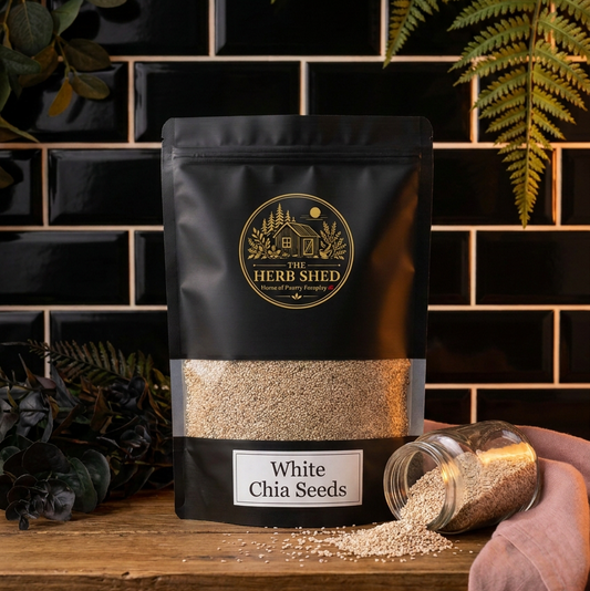 A clear glass jar filled with white chia seeds, featuring a silver metal lid and a cream-colored label that reads 'The Herb Shed' and 'White Chia Seeds'.