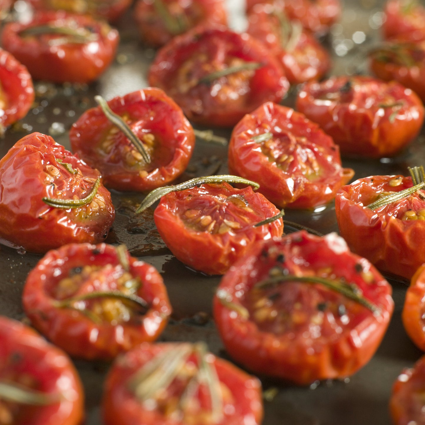 Roasted cherry tomatoes on a dark baking sheet, topped with olive oil, garlic, and rosemary.