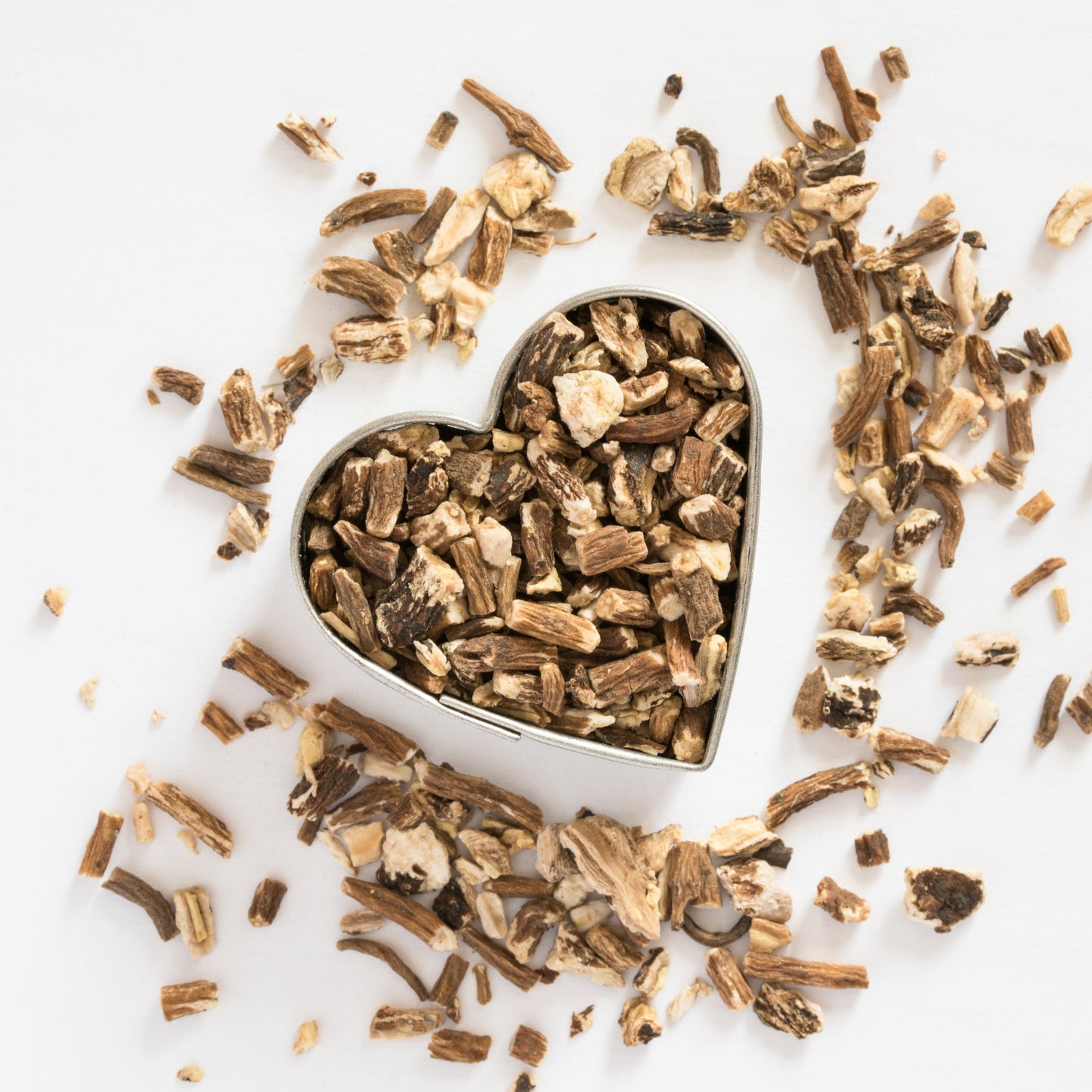 A heart-shaped metal mold filled with dried brown bark pieces, surrounded by scattered matching bark shavings on a plain white background.