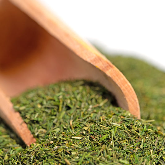 Wooden scoop filled with green tea leaves on a white background
