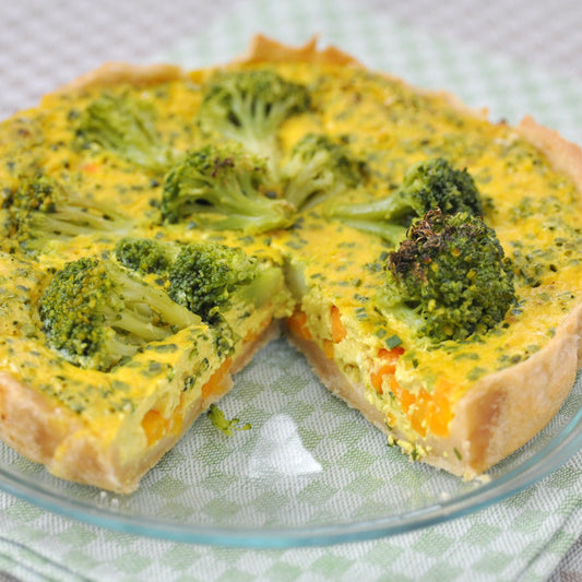 Quiche with broccoli and dill sprinkled on a glass plate on a checkered tablecloth