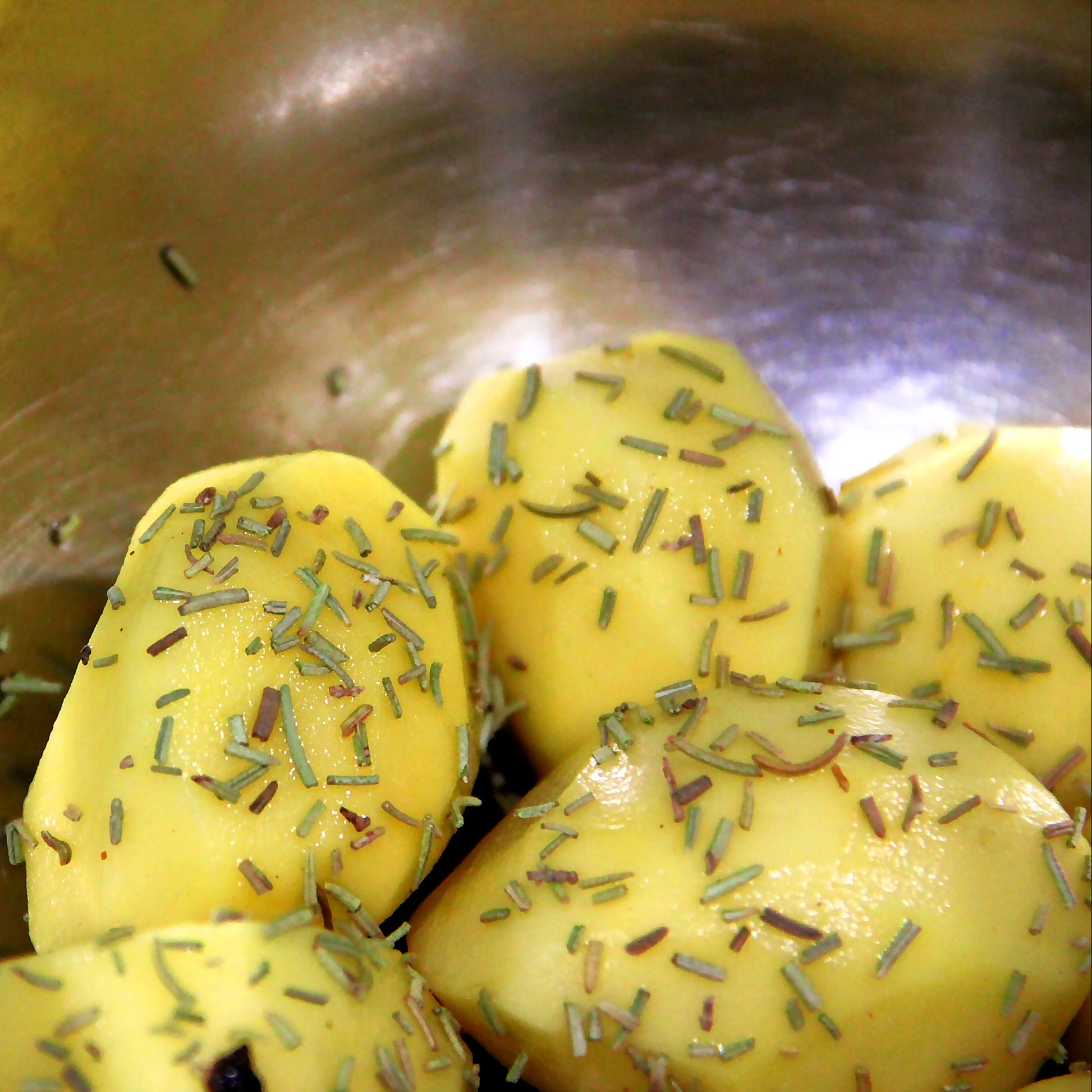 Yellow potato chunks seasoned with dried herbs inside a stainless steel bowl.
