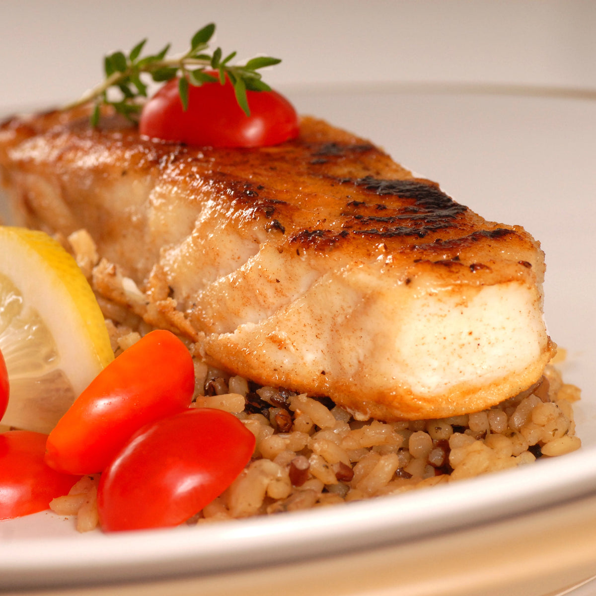 Grilled halibut served over brown rice with roasted tomatoes, lemon wedges and fresh herbs on a white plate, featuring Australian Brown Medium Grain Rice from The Herb Shed Wollongong Australia.