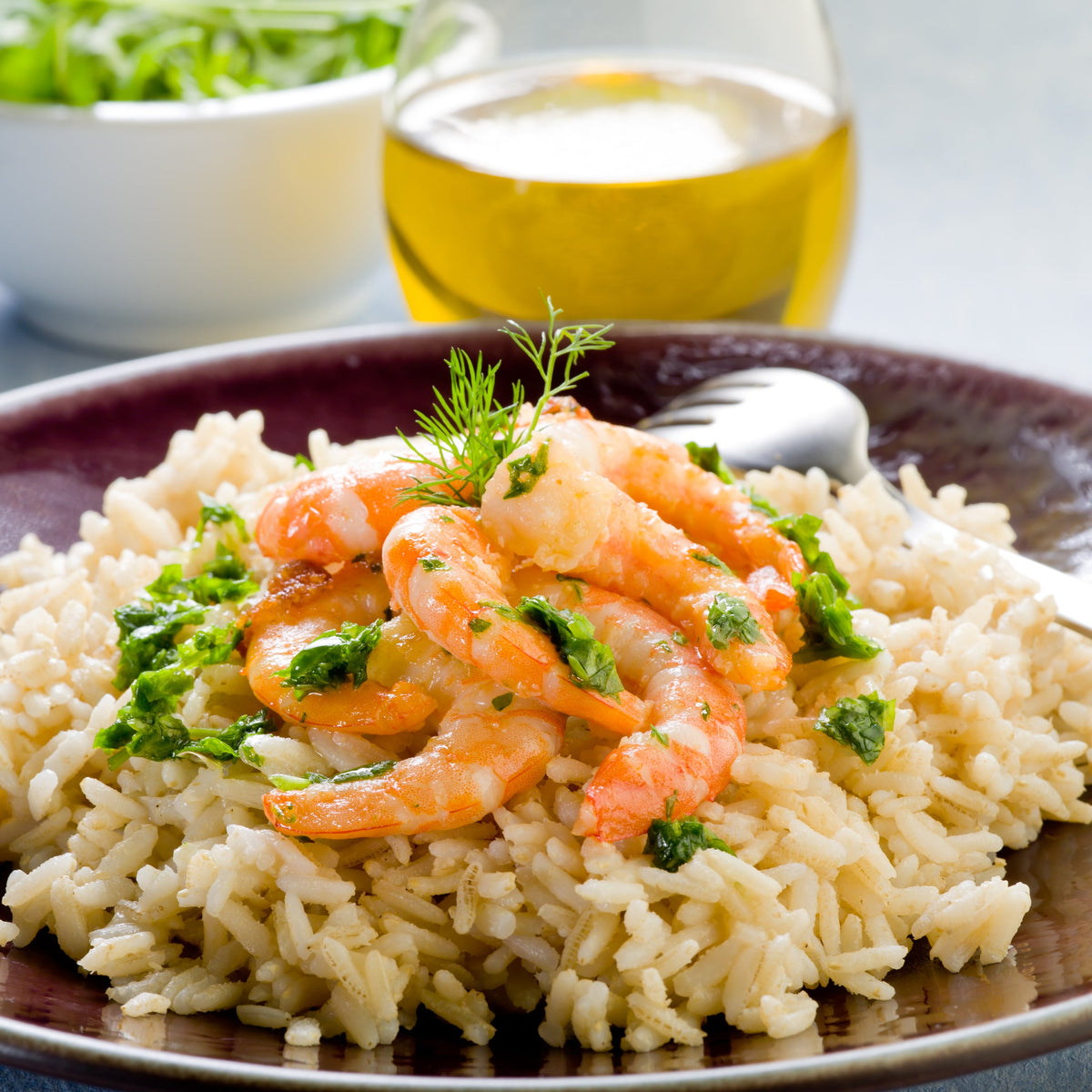 A colourful seafood rice dish with prawns, vegetables and fresh herbs served on a dark plate, featuring Australian Brown Medium Grain Rice from The Herb Shed Wollongong Australia.