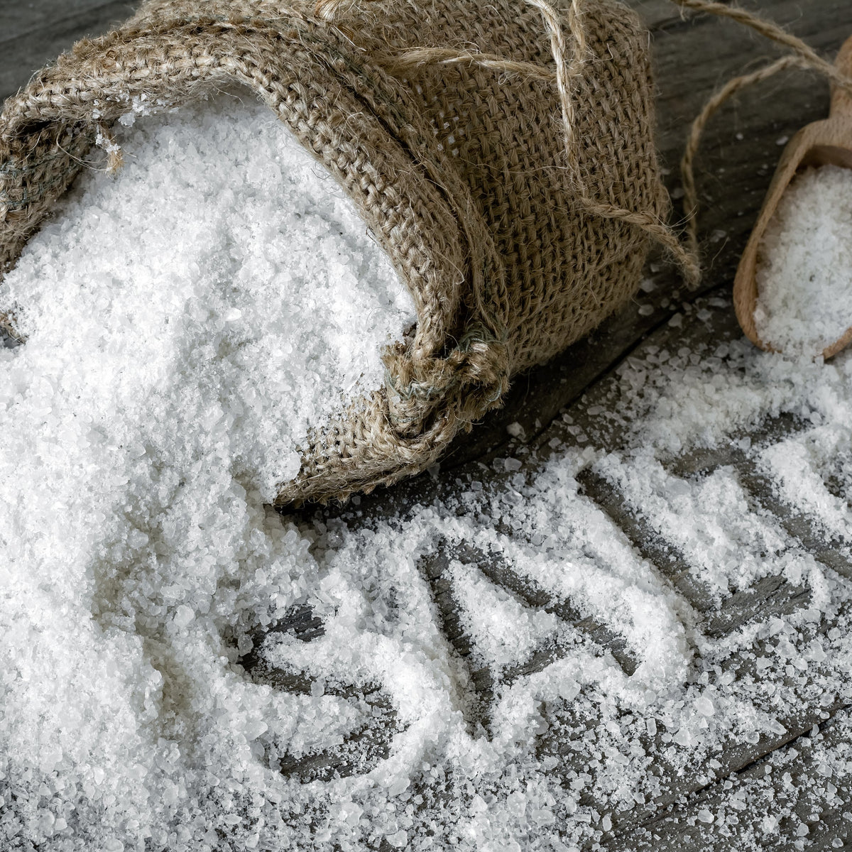 A close-up of fine white cooking salt spilling from a rustic sack, showing its small crystalline texture.
