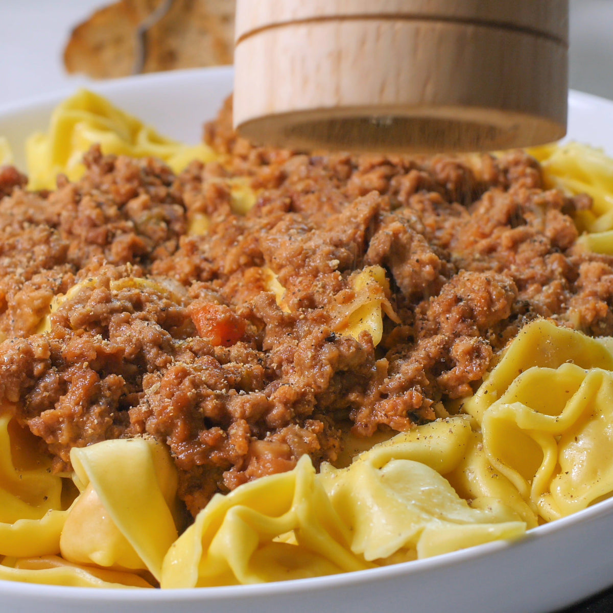 A bowl of ribbon pasta topped with a rich meat sauce and black pepper, showing Black Peppercorns used to season a savoury pasta dish.