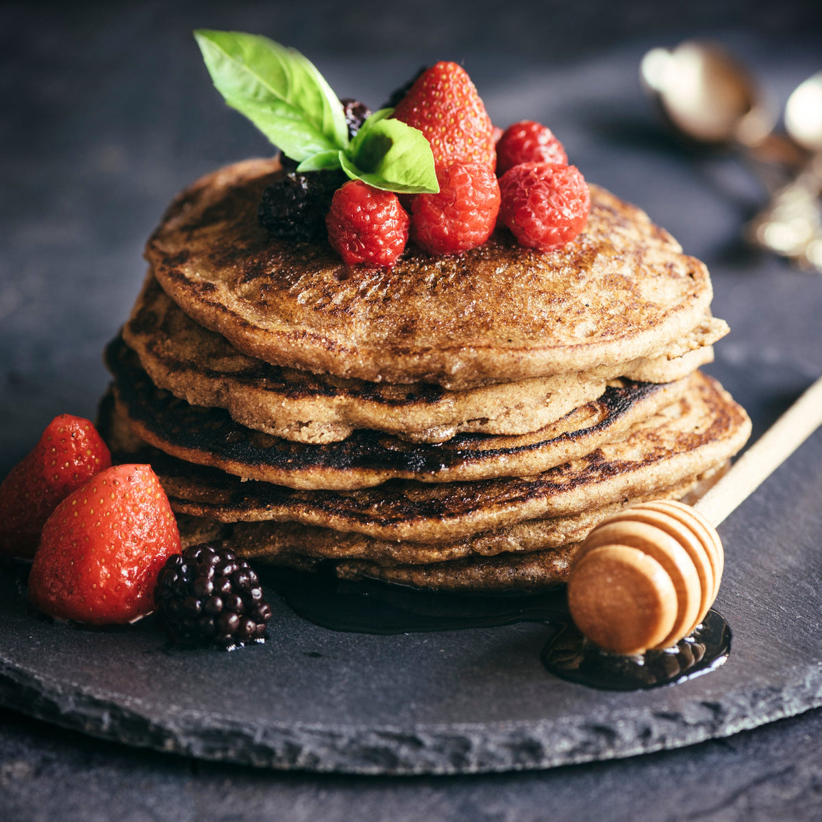 A stack of buckwheat pancakes topped with fresh berries and served with honey, showing Buckwheat Flour used for homemade pancakes.