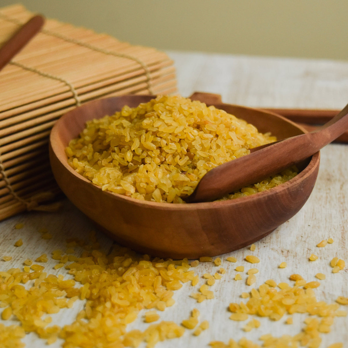 Cooked golden burghul fills a wooden bowl with a wooden spoon resting inside, showing the texture of Burghul Coarse after preparation.
