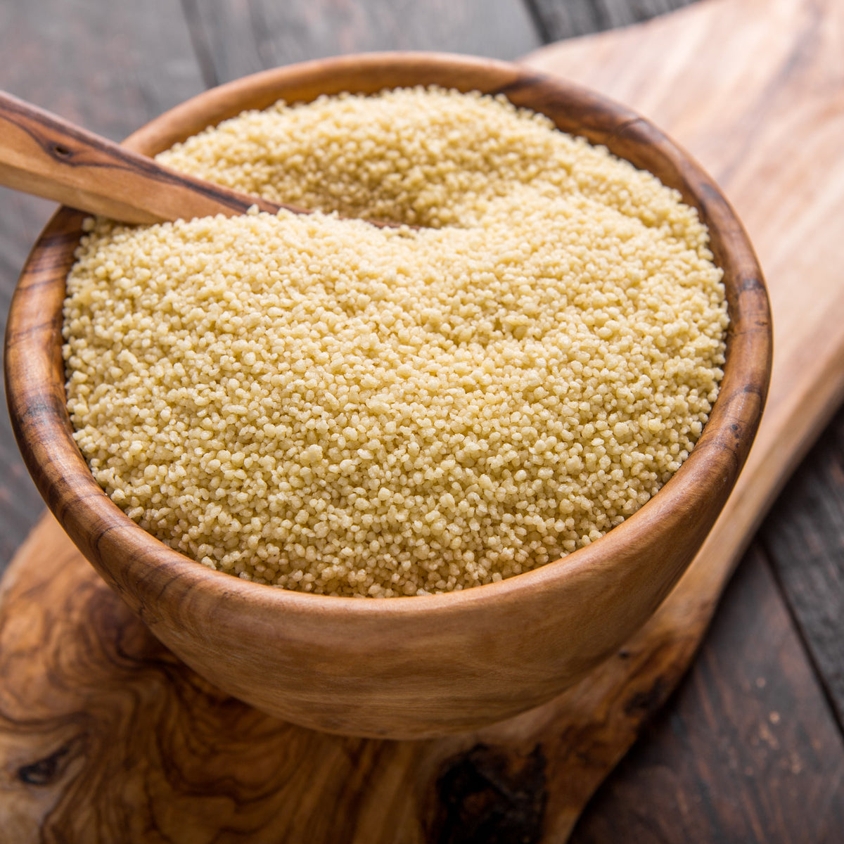 A rustic wooden bowl filled with fine golden burghul grains, with a wooden spoon resting inside on a dark timber surface, from The Herb Shed Wollongong Australia.