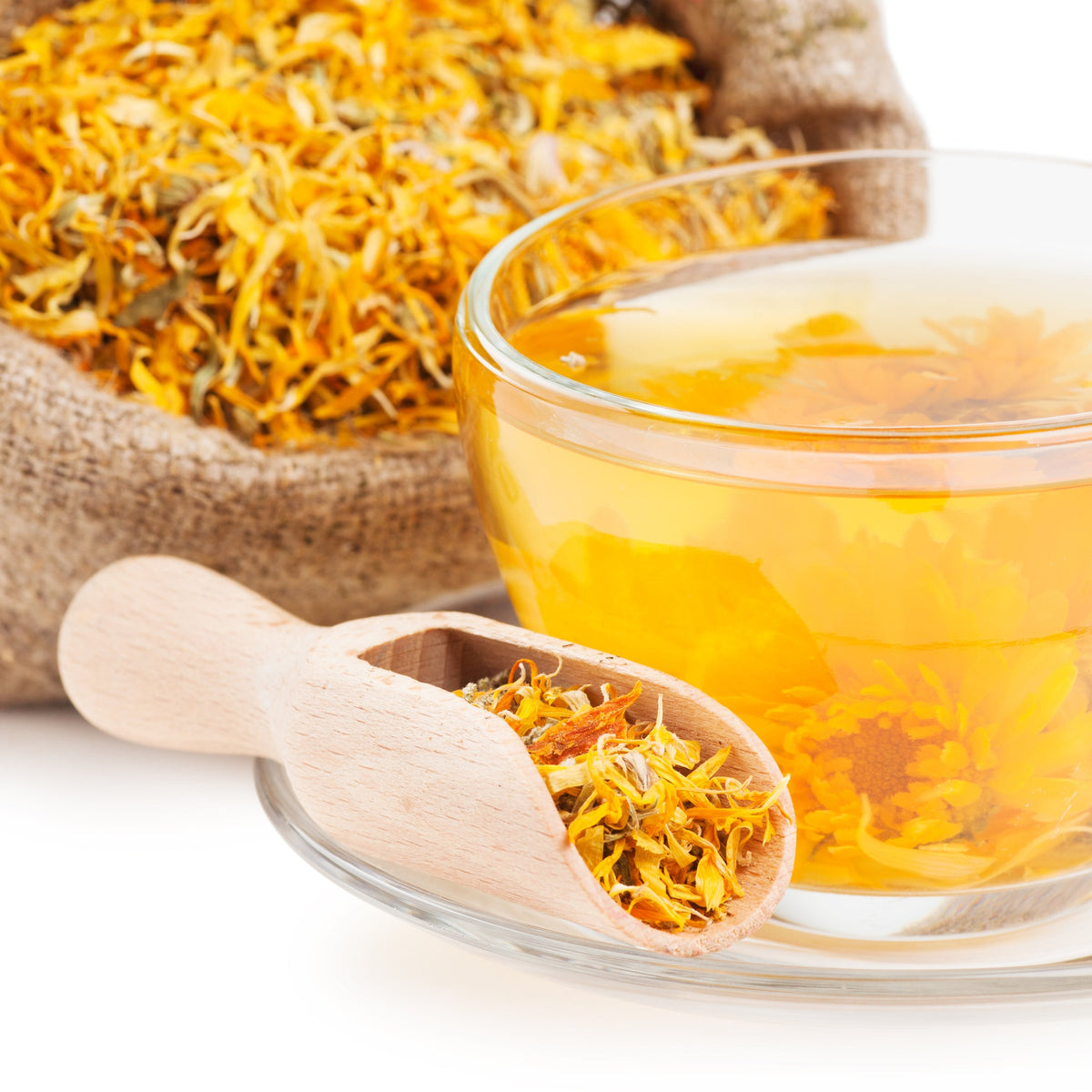 Golden calendula tea is served in a clear glass cup with dried calendula petals and a wooden scoop arranged beside it.