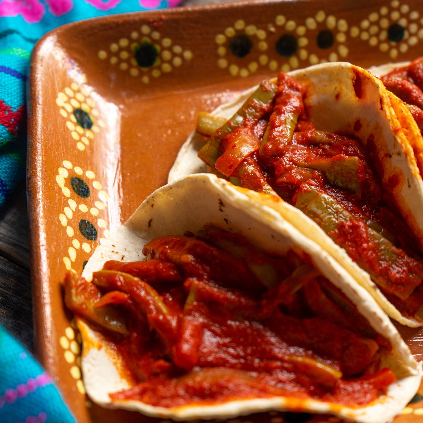 Soft tacos filled with meat and a rich red guajillo chilli sauce are served on a colourful plate, showing a cooking use for The Herb Shed Chilli Guajillo Dried.