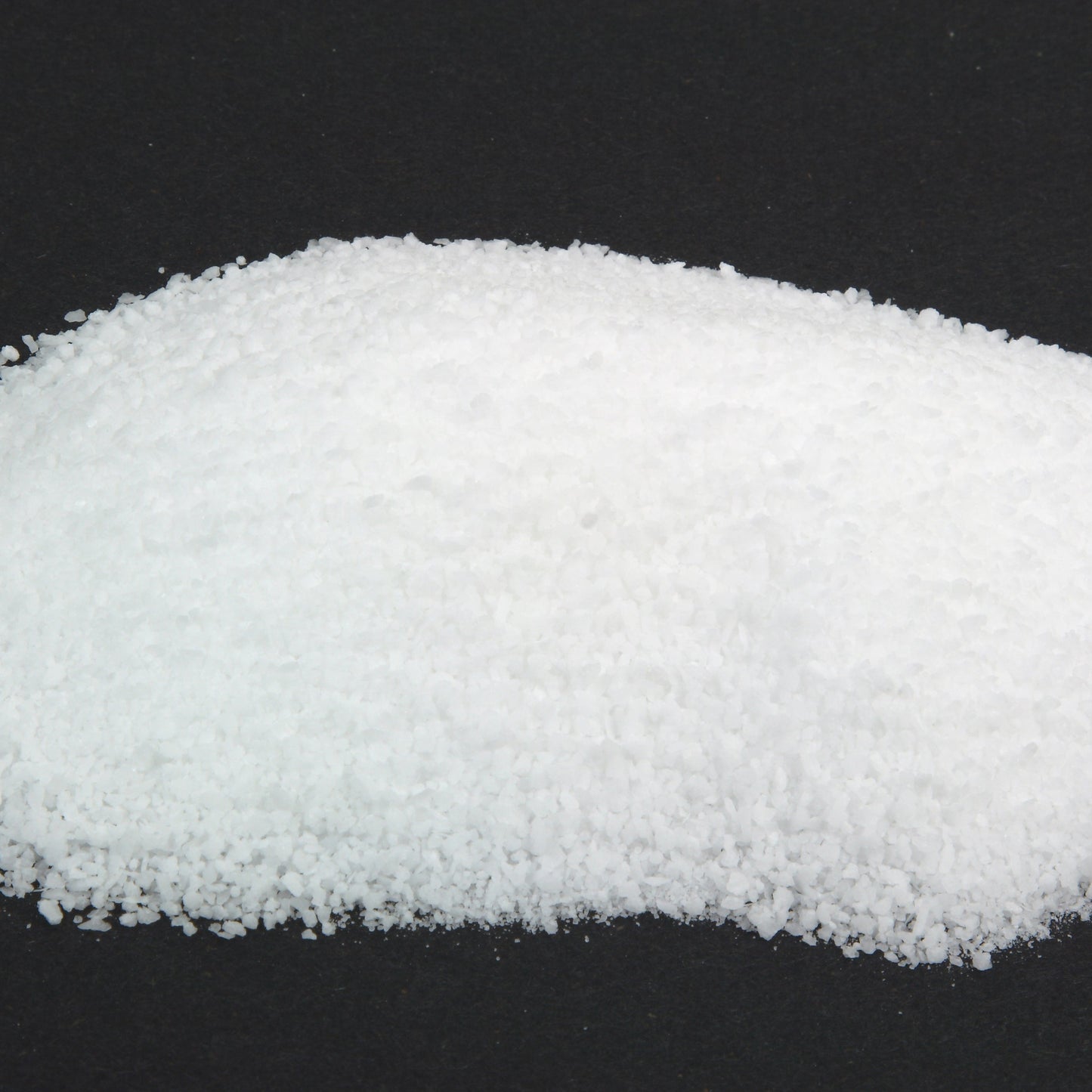 A close-up mound of fine white pickling salt against a dark background shows the fine, even texture of the salt.