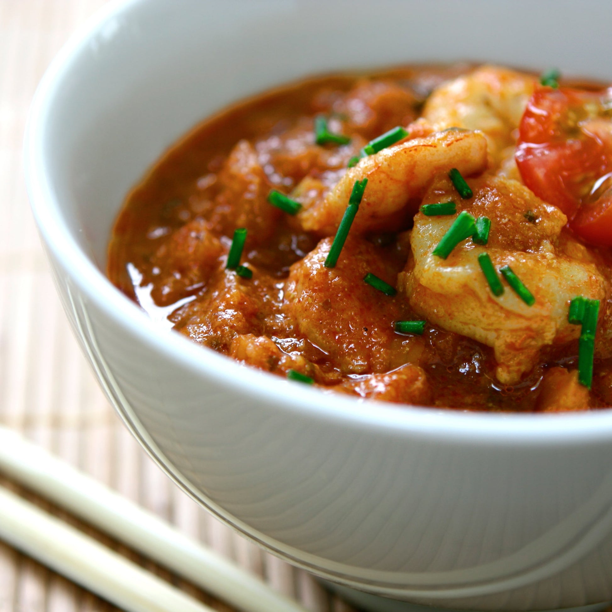 A rich tomato-based curry seasoned with cumin is served in a white bowl and garnished with fresh green herbs.