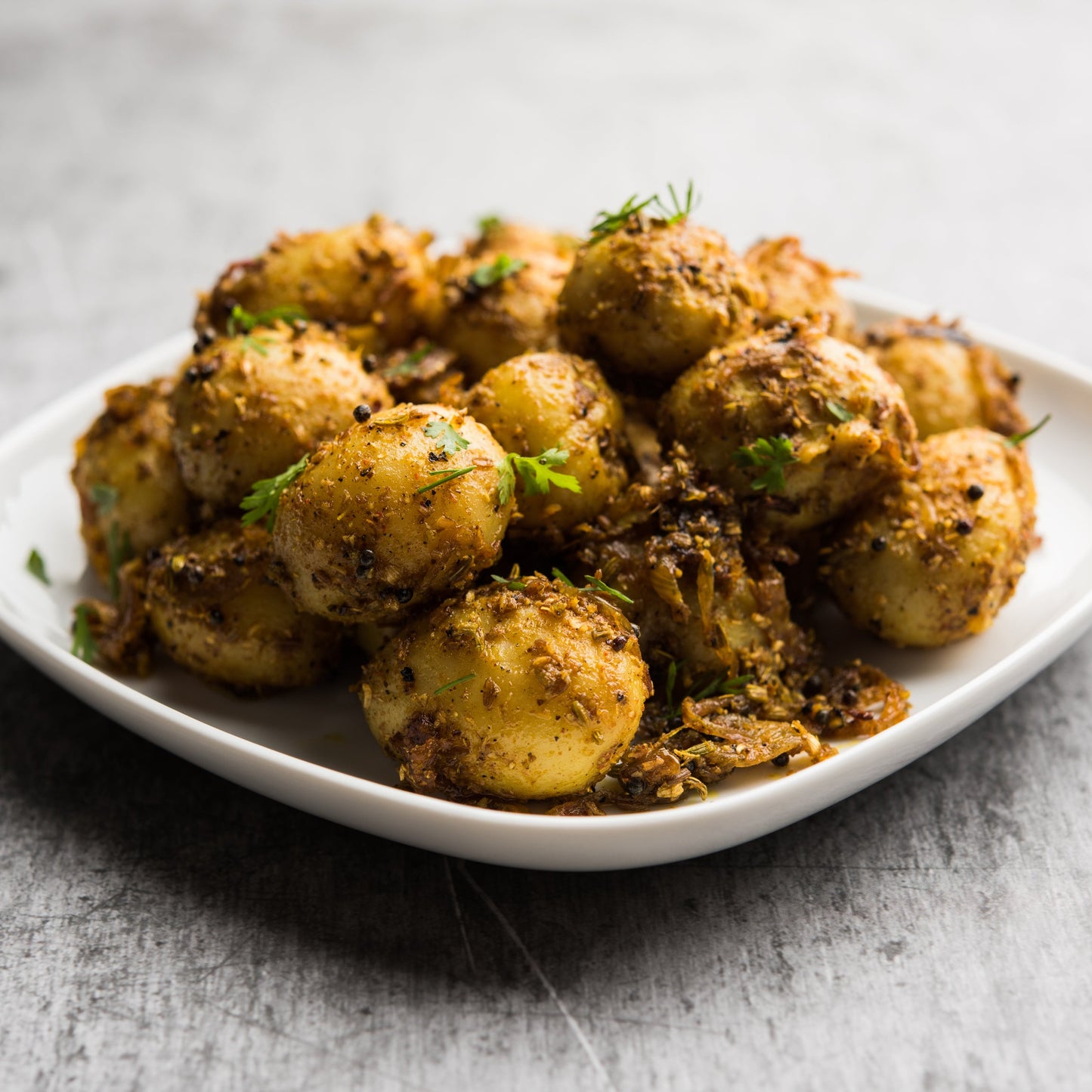 Golden roasted potatoes seasoned with cumin seeds are served on a dark plate, showing a savoury cooking idea using The Herb Shed Cumin Seeds.