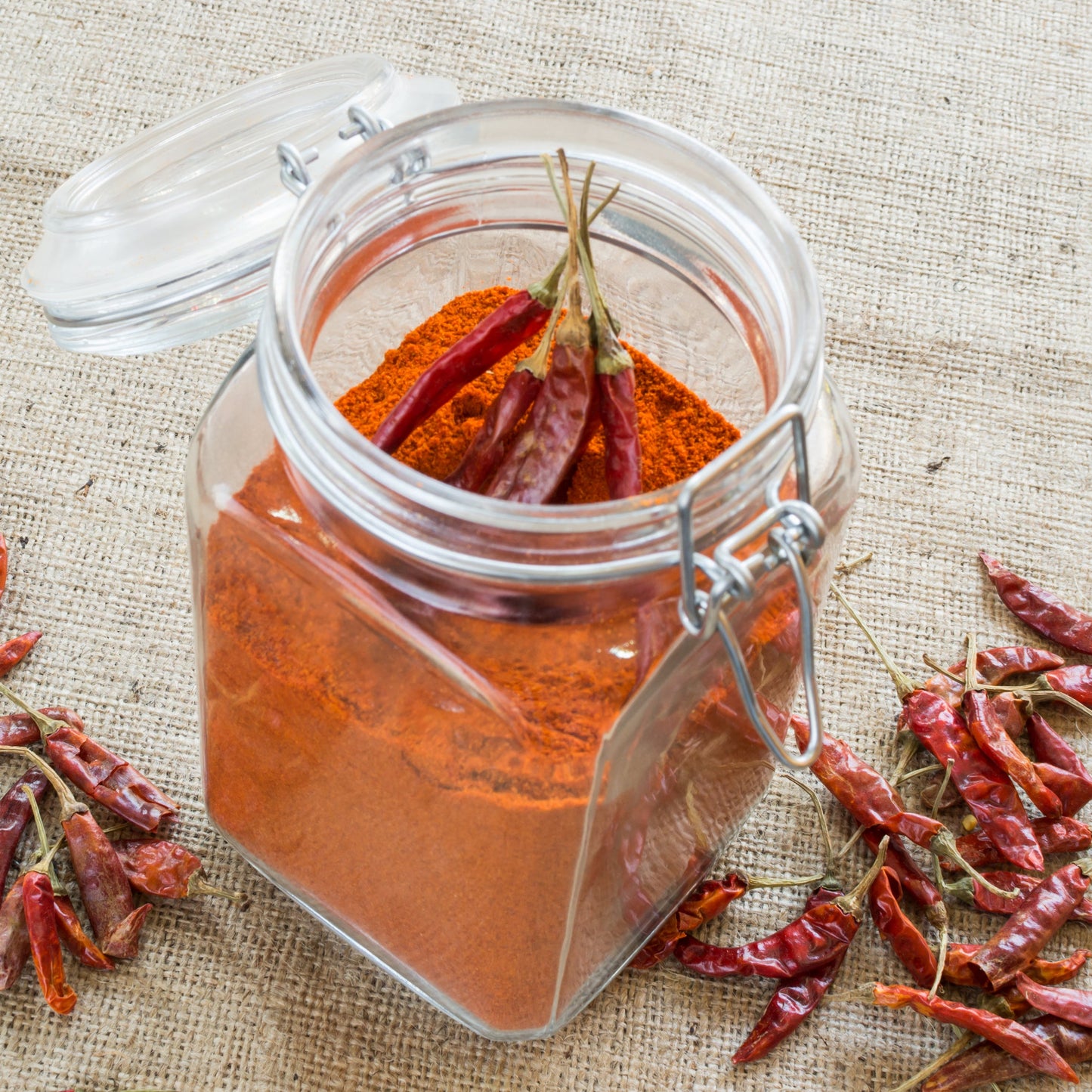 Ground red chilli fills a small glass jar surrounded by whole dried Birds Eye chillies, showing another way the dried chilli pods can be prepared for cooking.