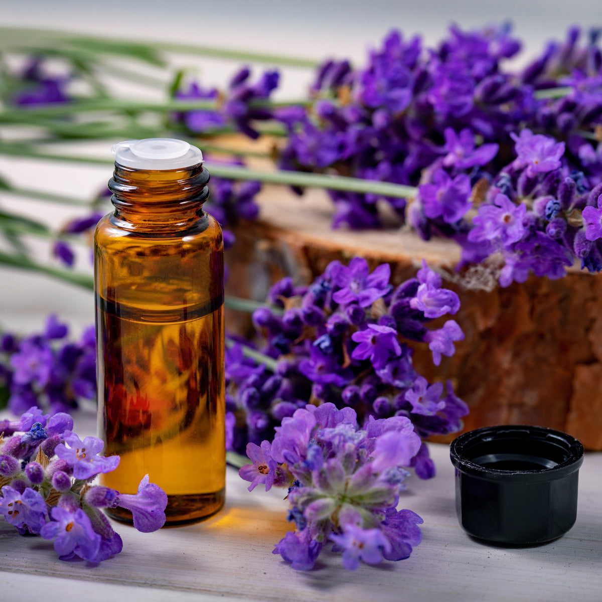 An amber bottle of lavender oil surrounded by purple lavender flowers, representing a traditional aromatic use associated with Dried Lavender Flowers from The Herb Shed in Wollongong, Australia.