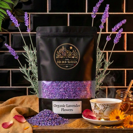 A black stand-up pouch of The Herb Shed Dried Lavender Flowers in Wollongong, Australia, sits on a wooden surface with loose lavender flowers, fresh lavender stems and a teacup against a black tiled background.