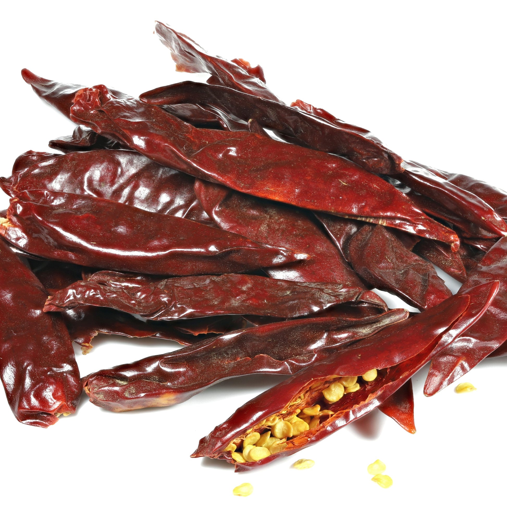 Whole dried Teja chilli pods are arranged against a white background, showing their long tapered shape, wrinkled skin and deep red colour, with a split chilli revealing the seeds inside.