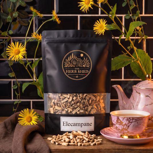 A black stand-up pouch of The Herb Shed Elecampane in Wollongong, Australia, sits on a wooden surface with loose dried elecampane root and a cup of herbal tea, surrounded by yellow flowers and warm brown fabric against a black tiled background.