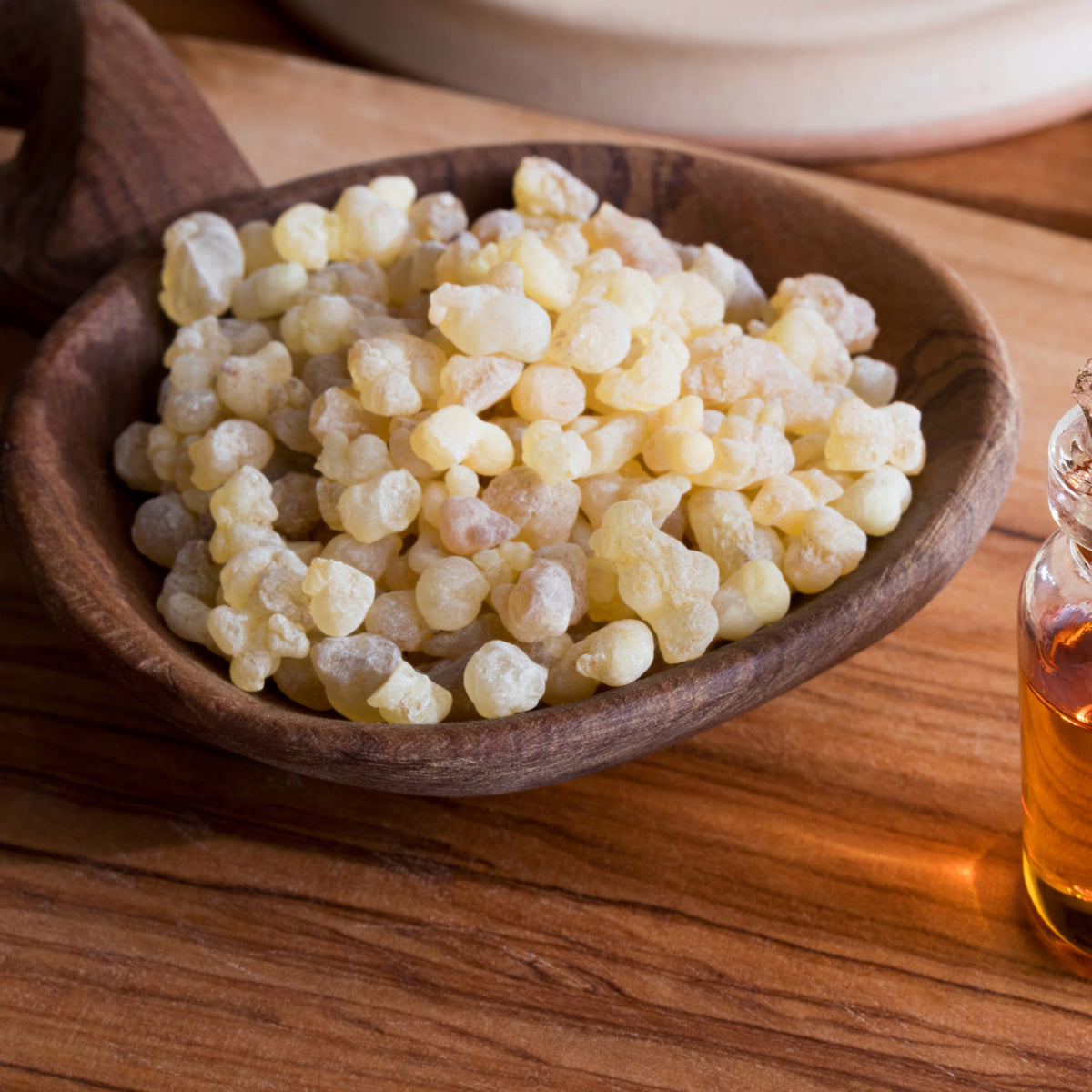 Pale golden frankincense resin pieces fill a wooden spoon on a timber surface, showing the irregular shape and natural translucent colouring of the resin.