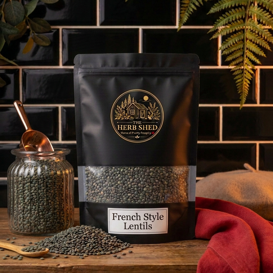 A black stand-up pouch of The Herb Shed French Style Lentils in Wollongong, Australia, sits on a wooden surface with loose lentils and a glass jar, surrounded by greenery and deep red fabric against a black tiled background.