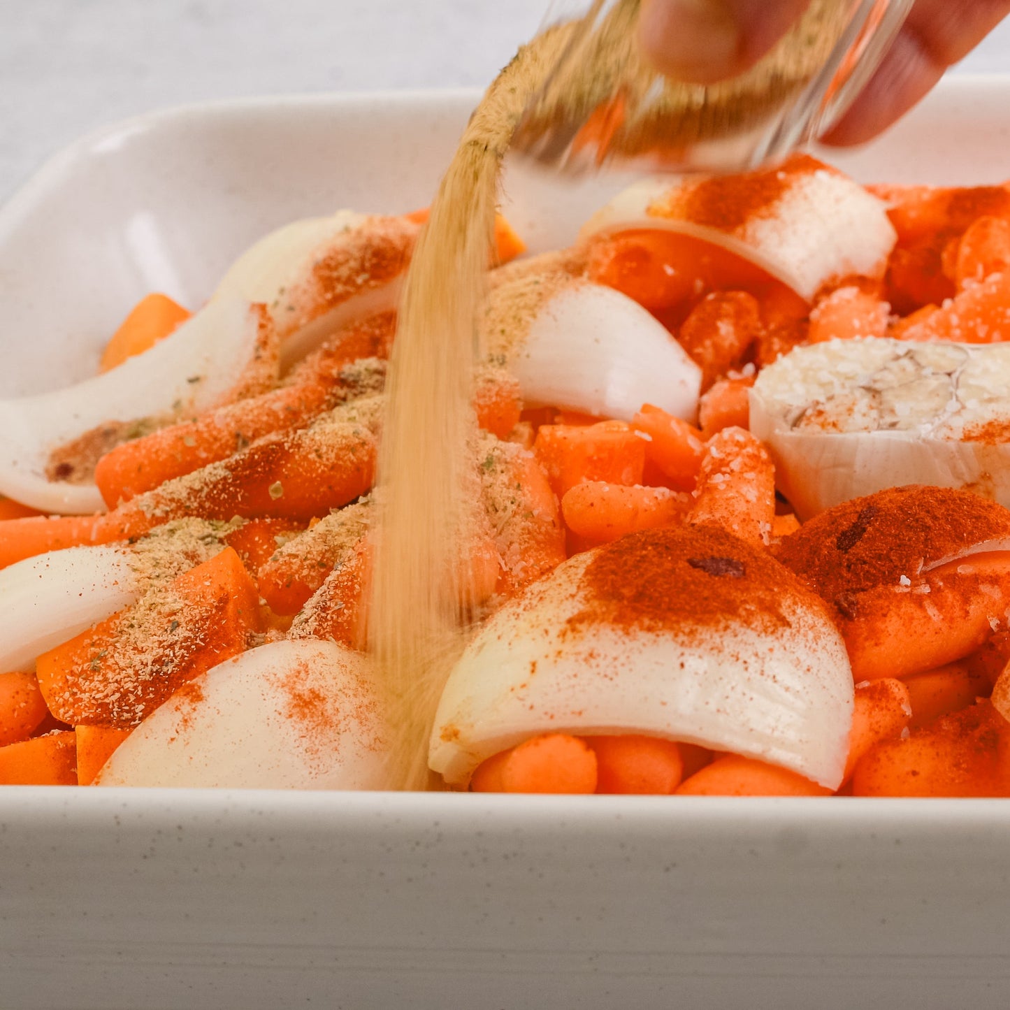 Garlic powder is being sprinkled over sliced vegetables in a baking dish, showing The Herb Shed Garlic Powder being used as a seasoning before cooking.