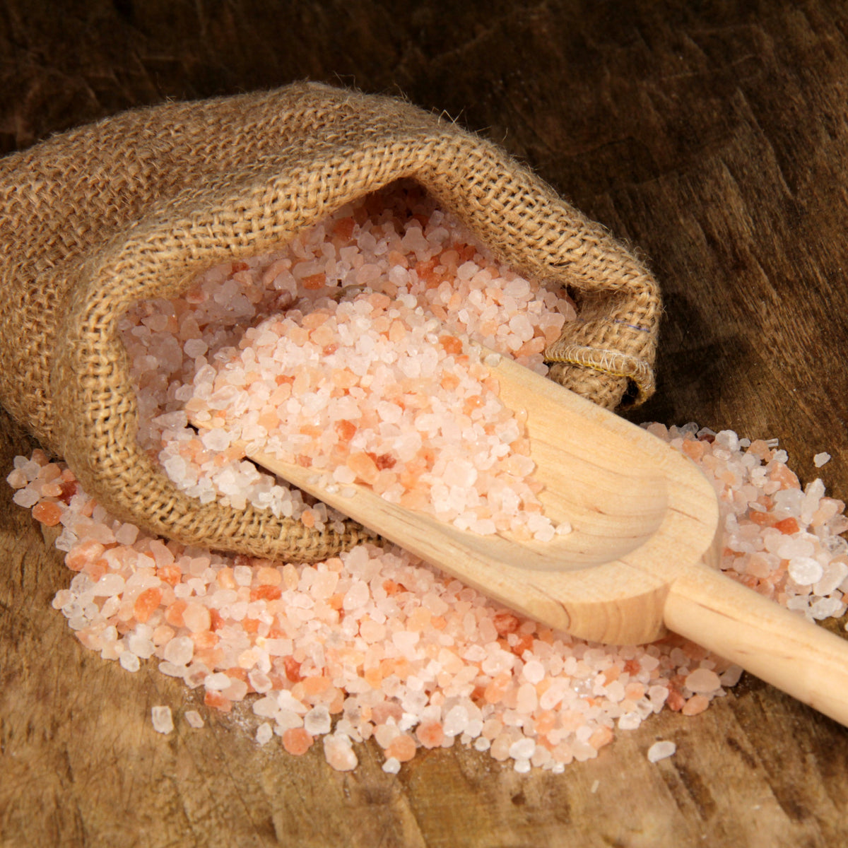 Coarse Himalayan Pink Salt crystals spilling from a wooden scoop onto rustic hessian fabric, from The Herb Shed Wollongong Australia.