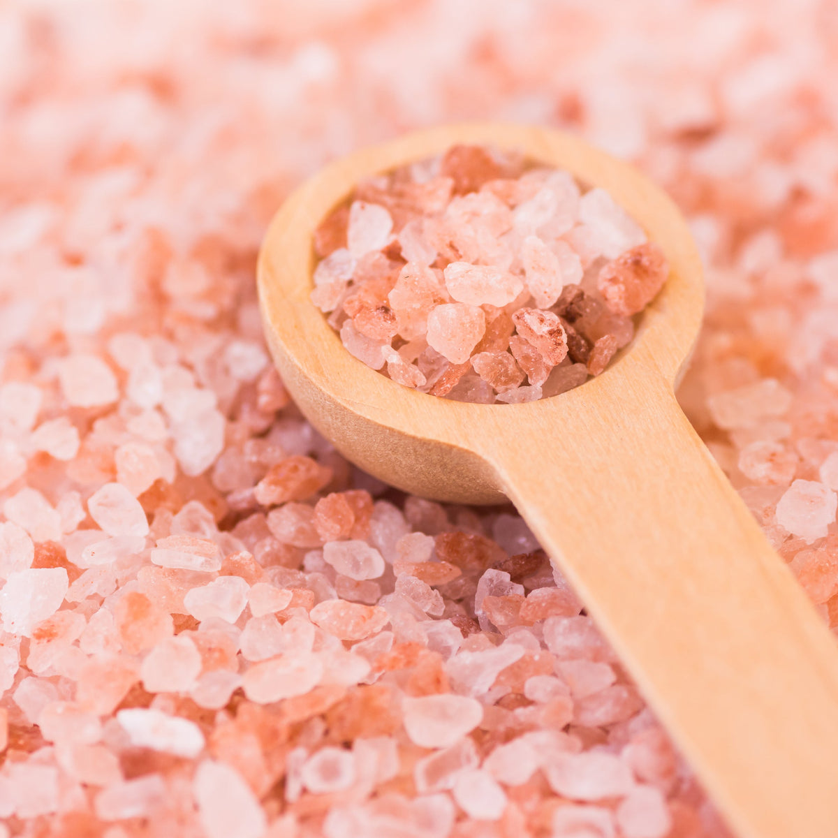 A wooden spoon resting among coarse Himalayan Pink Salt crystals in shades of soft pink and white, from The Herb Shed Wollongong Australia.