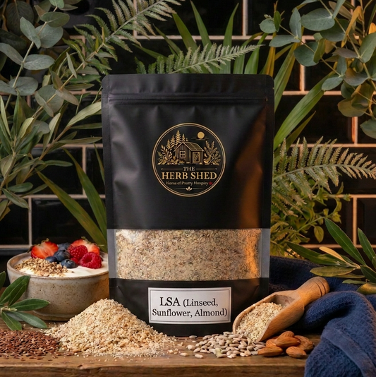 A black stand-up pouch of The Herb Shed LSA Linseed, Sunflower and Almond in Wollongong, Australia, sits on a wooden surface with loose LSA, linseeds, sunflower seeds and almonds, surrounded by greenery against a black tiled background.