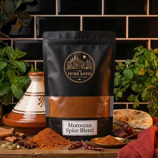 A black stand-up pouch of The Herb Shed Moroccan Spice Blend in Wollongong, Australia, sits on a wooden surface with loose spice, whole spices, fresh herbs and Moroccan-inspired tableware against a black tiled background.