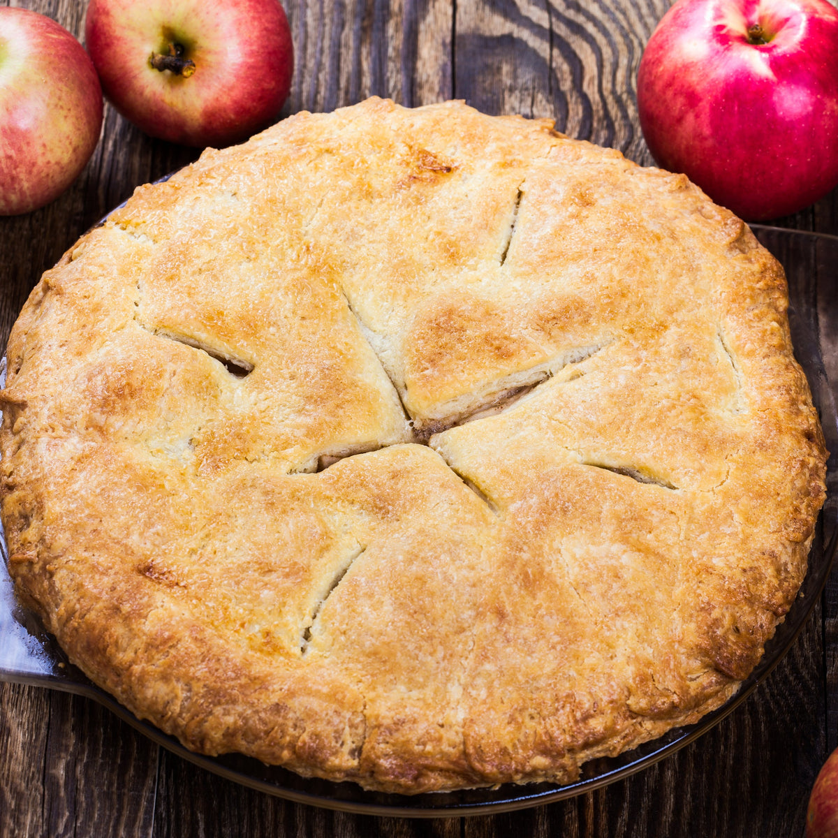 A freshly baked golden apple pie sits beside red apples, showing Organic Allspice used in sweet baking and spiced desserts.