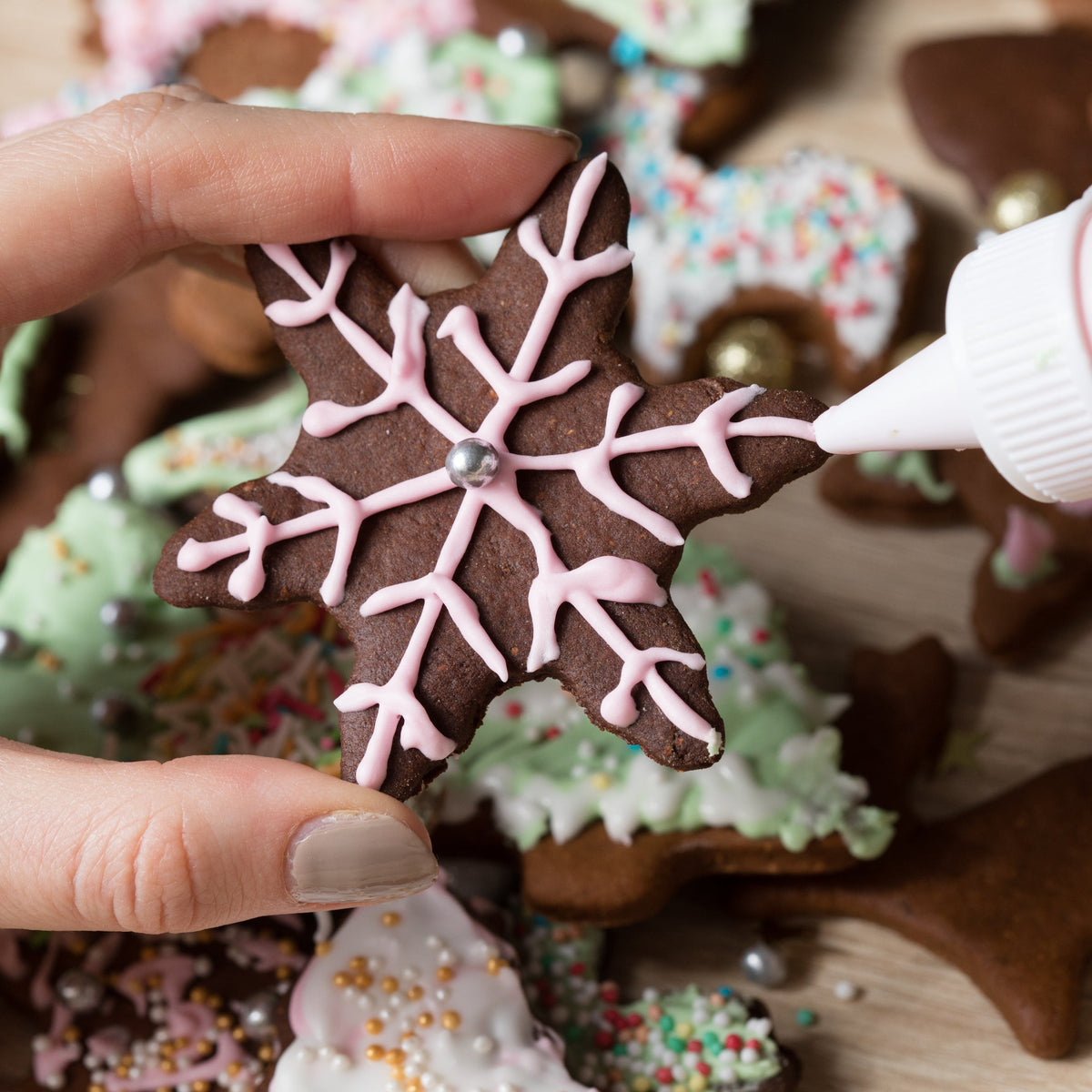 Decorated gingerbread biscuits are being finished with white icing, showing Organic Allspice used in warmly spiced baking.
