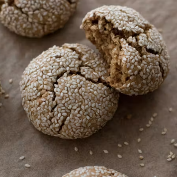 Freshly baked cracked biscuits made with aniseed are arranged on a surface with loose seeds scattered around them.