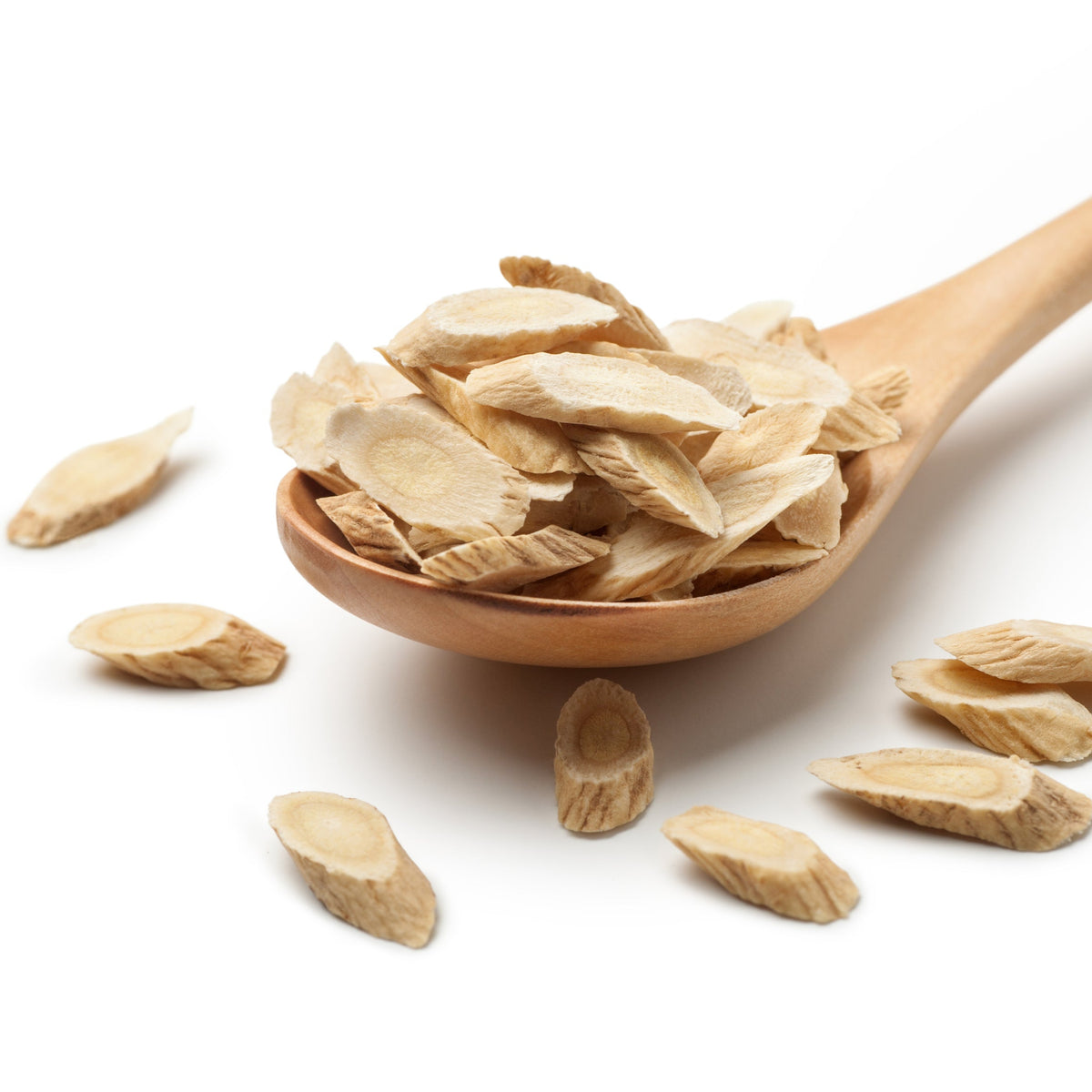 Dried Organic Astragalus Root pieces fill a wooden spoon with several pieces scattered around it against a white background.