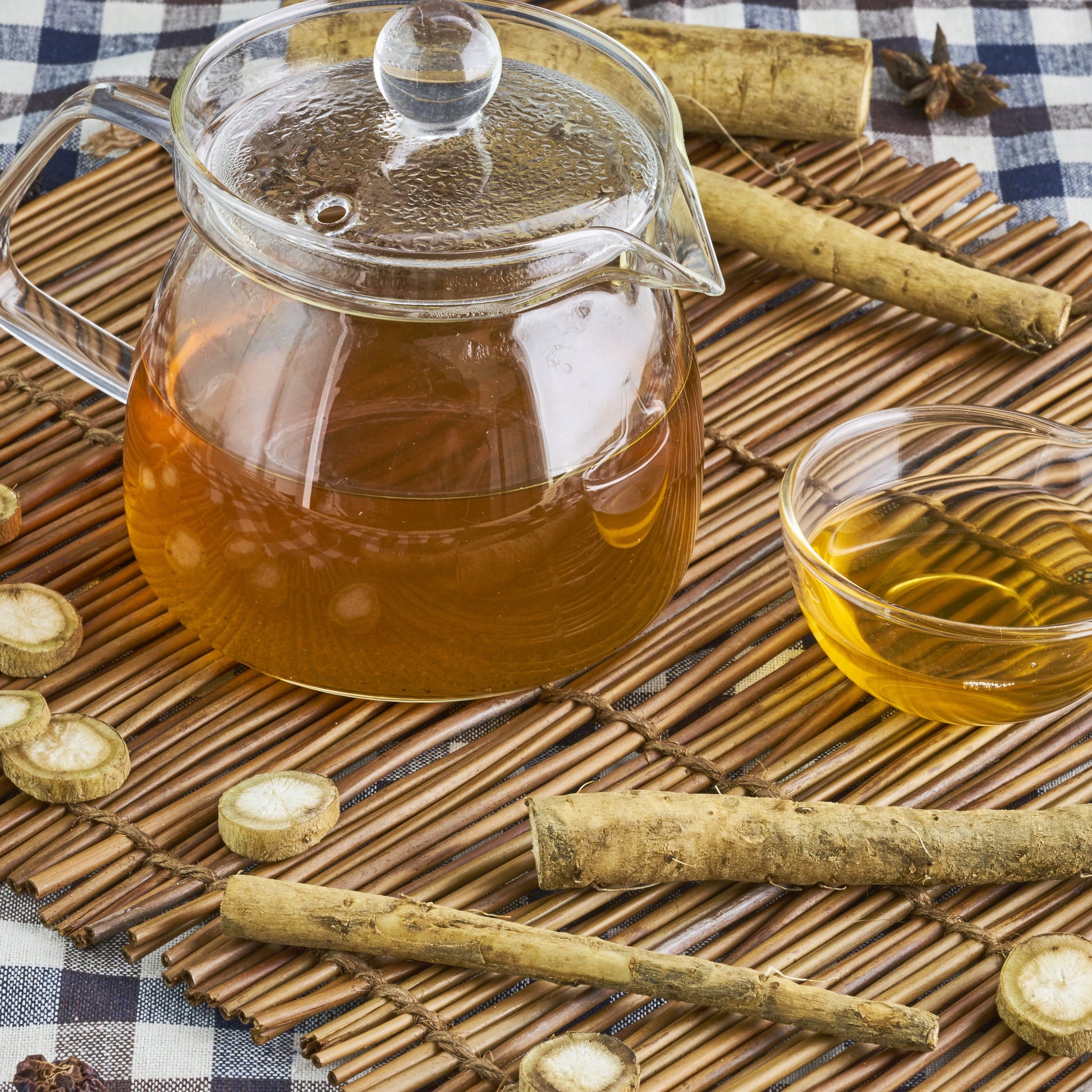 Brewed burdock root tea is served in a clear glass teapot and cup on a rustic table, with dried burdock root pieces arranged nearby.