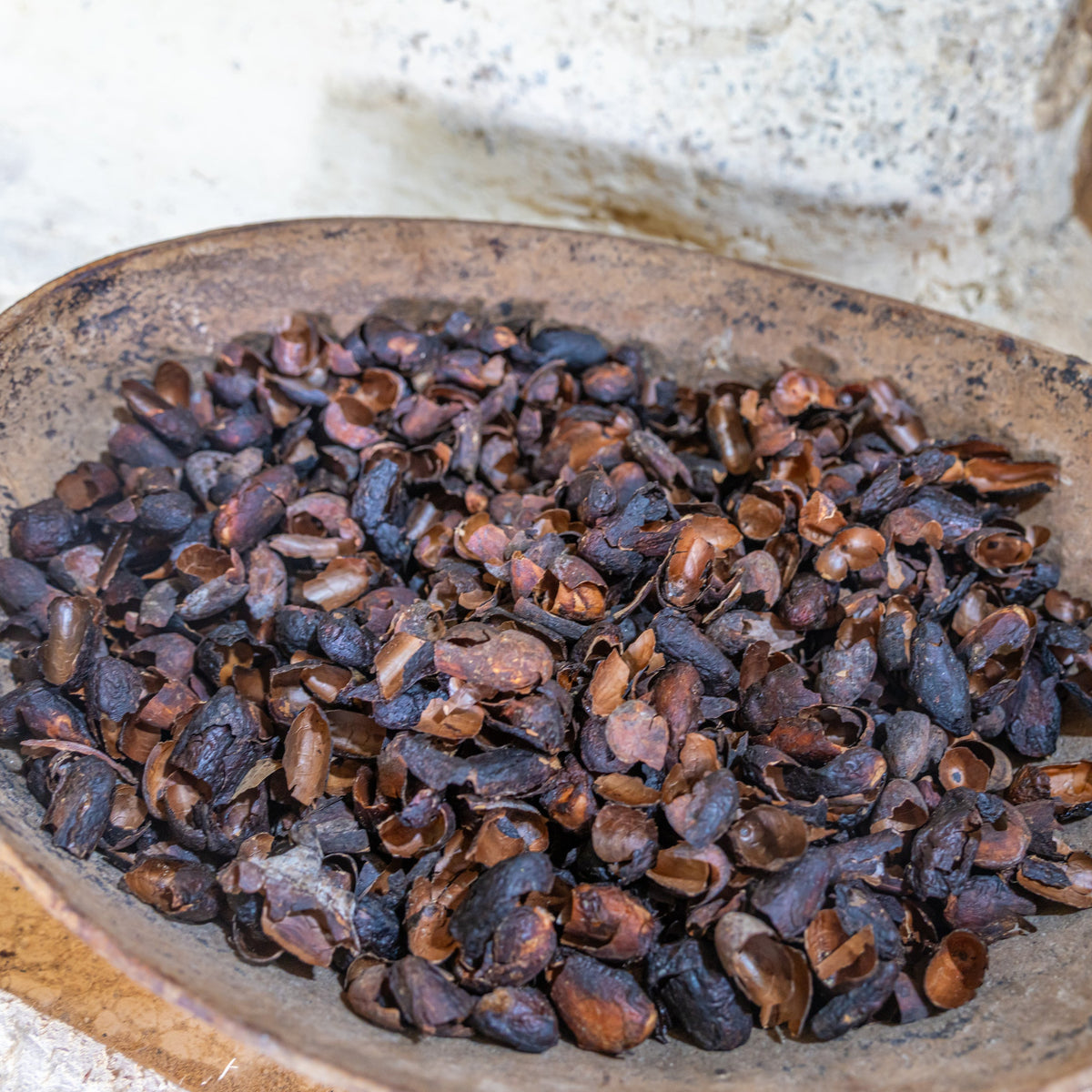 A close-up of Organic Cacao Husks in a rustic bowl, showing the curled dried pieces and their natural deep brown colouring and texture.