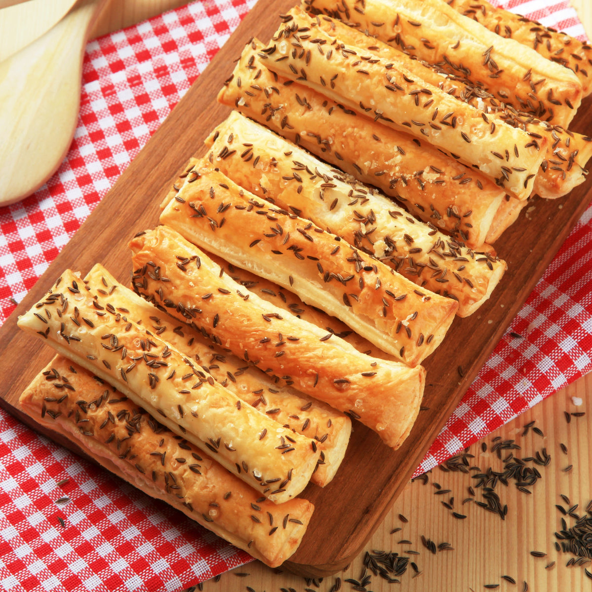 Slices of freshly baked bread topped with caraway seeds are arranged on a wooden board, showing a baking use for The Herb Shed Organic Caraway Seeds.