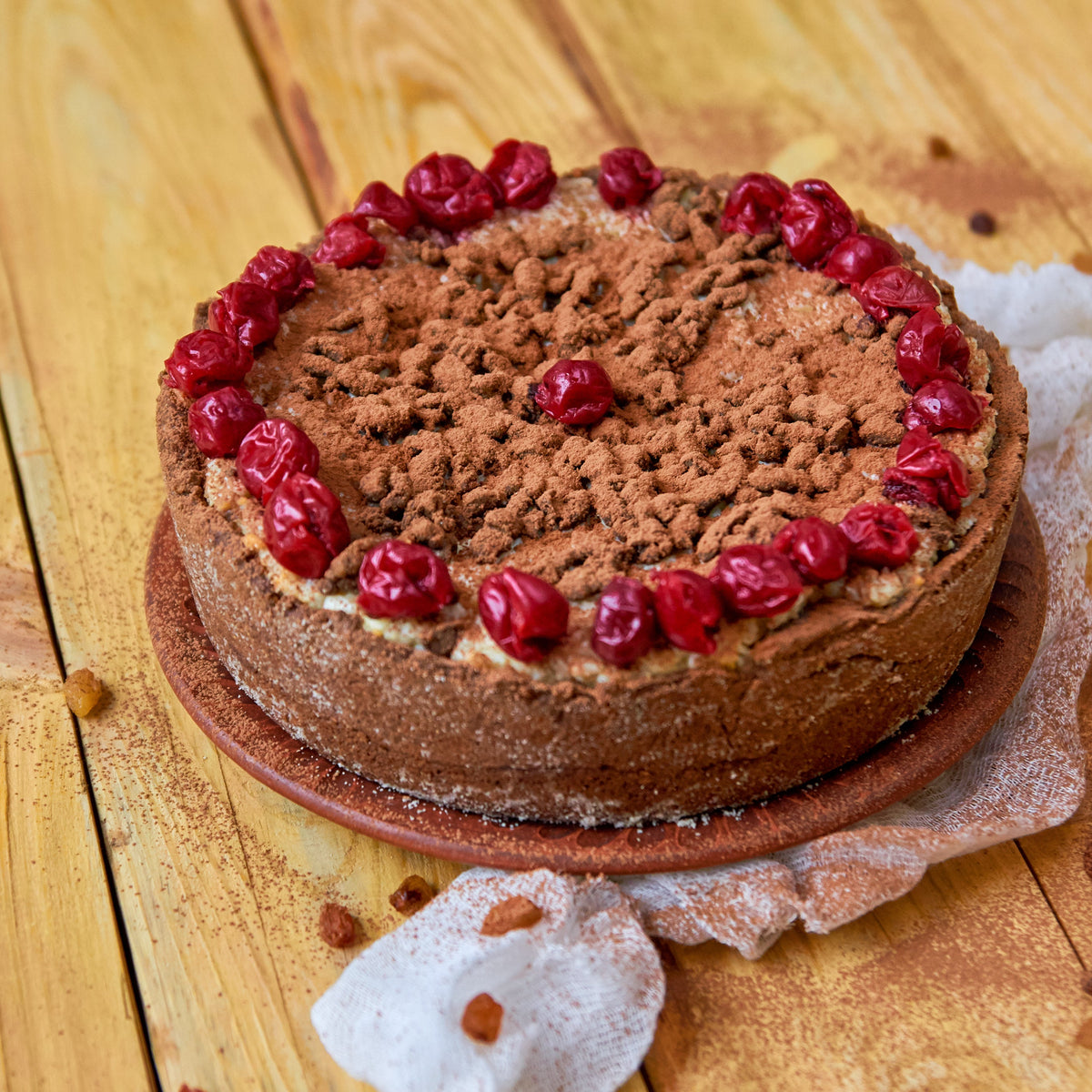 A round carob cake topped with creamy carob frosting and fresh raspberries sits on a wooden surface, showing a dessert use for The Herb Shed Organic Roasted Carob Powder.
